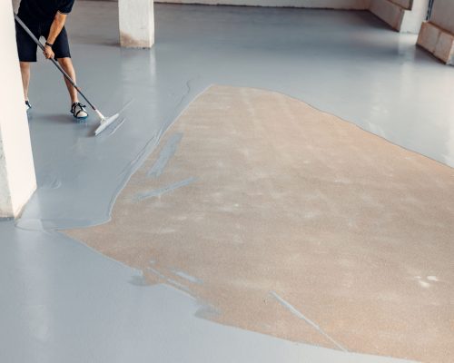 A construction worker apply grey epoxy resin in an industrial hall